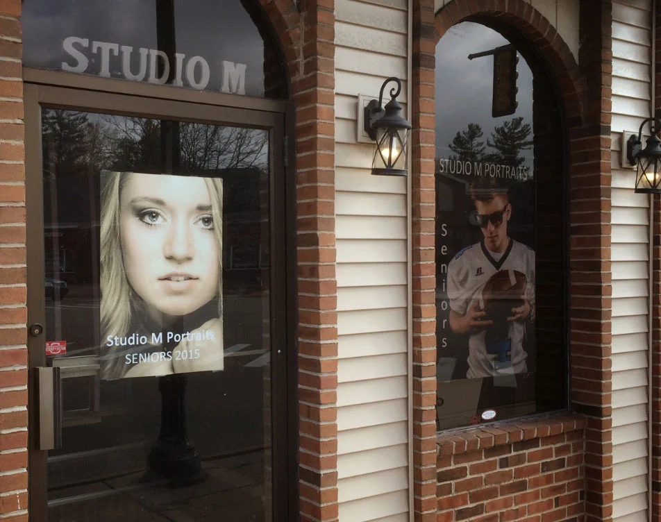 The Studio M shopfront, with senior portrait prints displayed in the glass door and side window beneath the STUDIO M sign